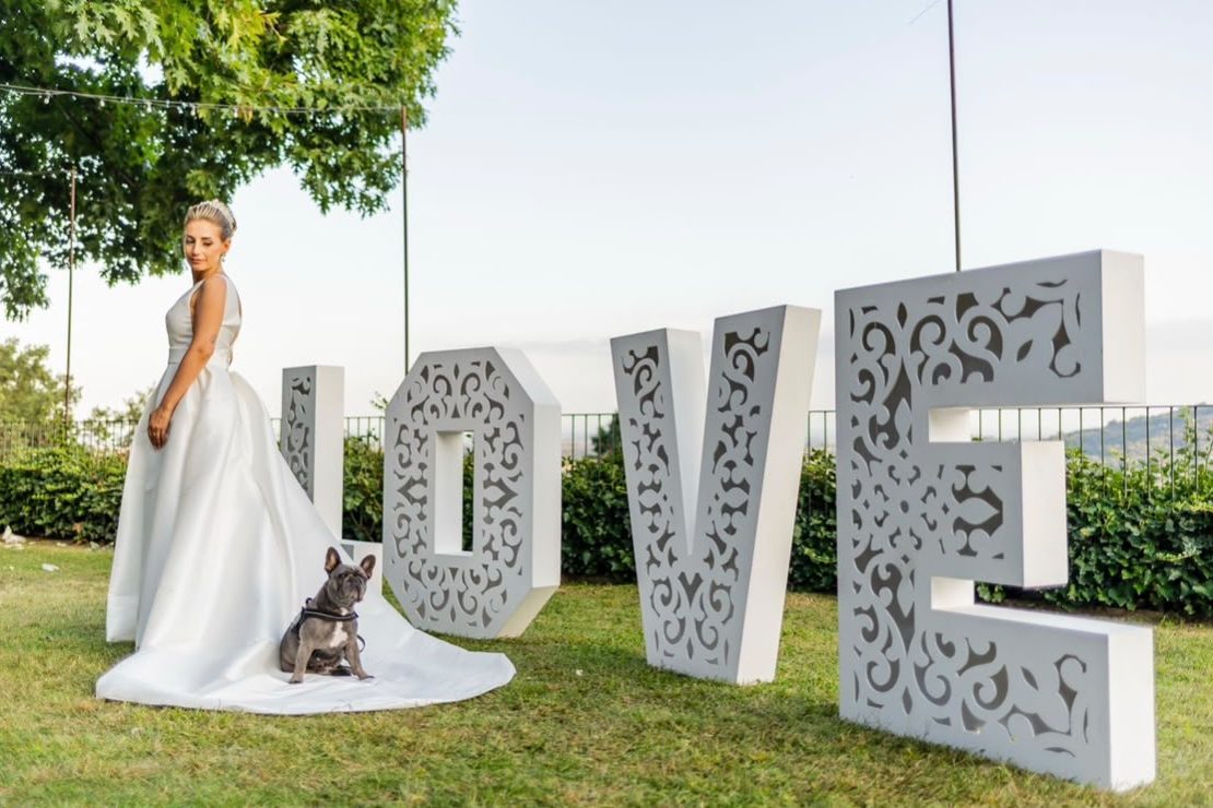 La sposa nel prato accanto alle grandi lettere LOVE, con il bouledogue francese seduto sullo strascico