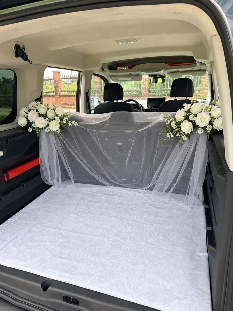 Bagagliaio dell’auto allestito con velo bianco e mazzi di rose per accompagnare il cane al matrimonio