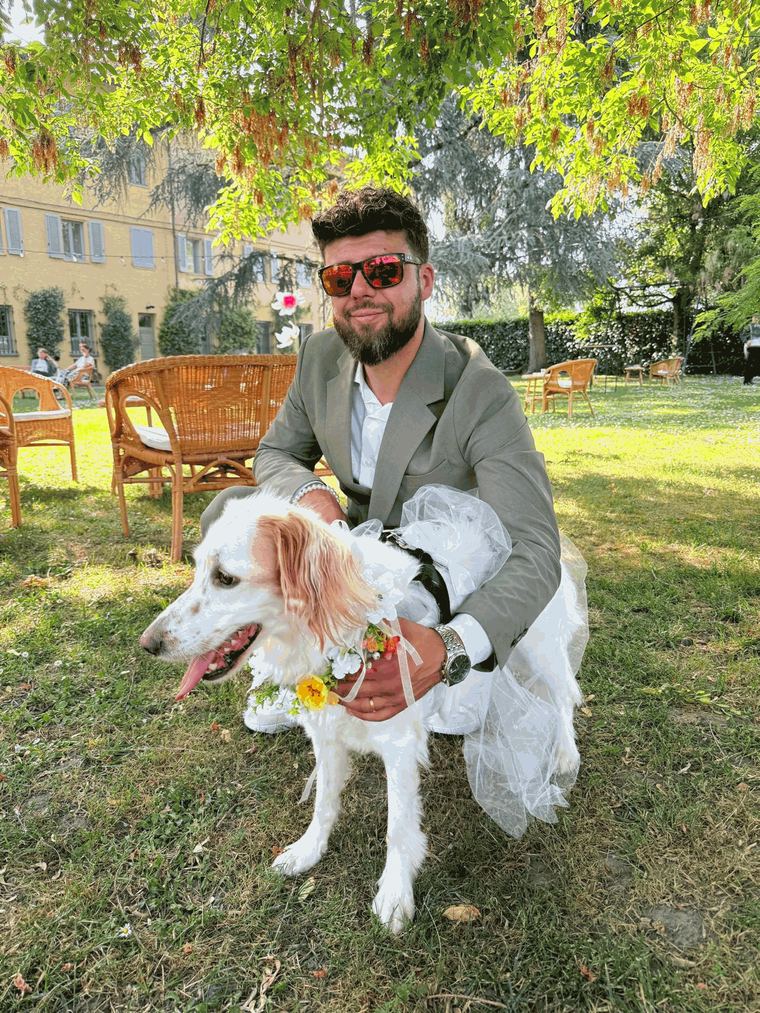 Davide inginocchiato abbraccia un setter vestito da sposa con collare di fiori, durante un matrimonio